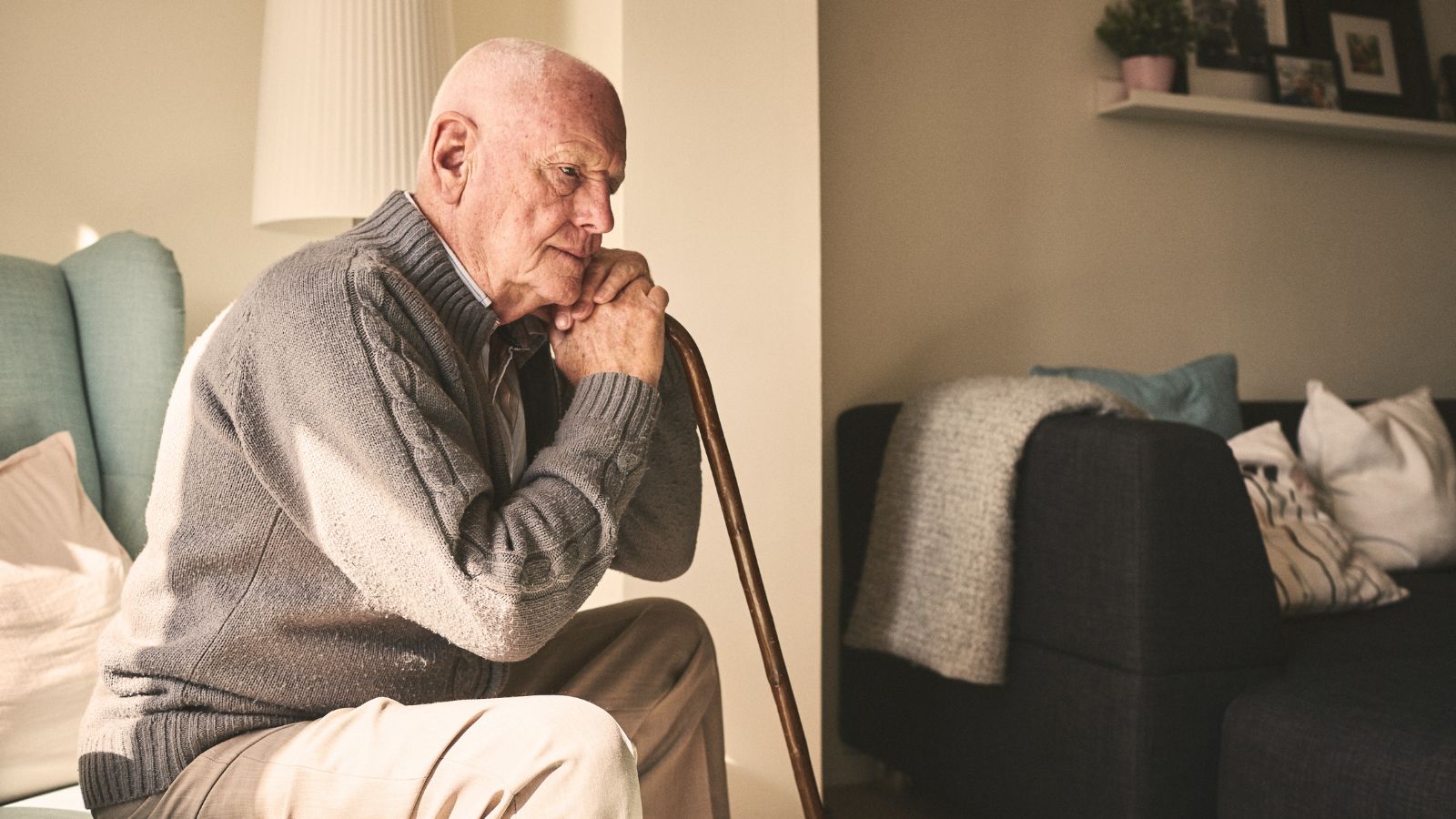 Older male sat on the sofa with a walking stick